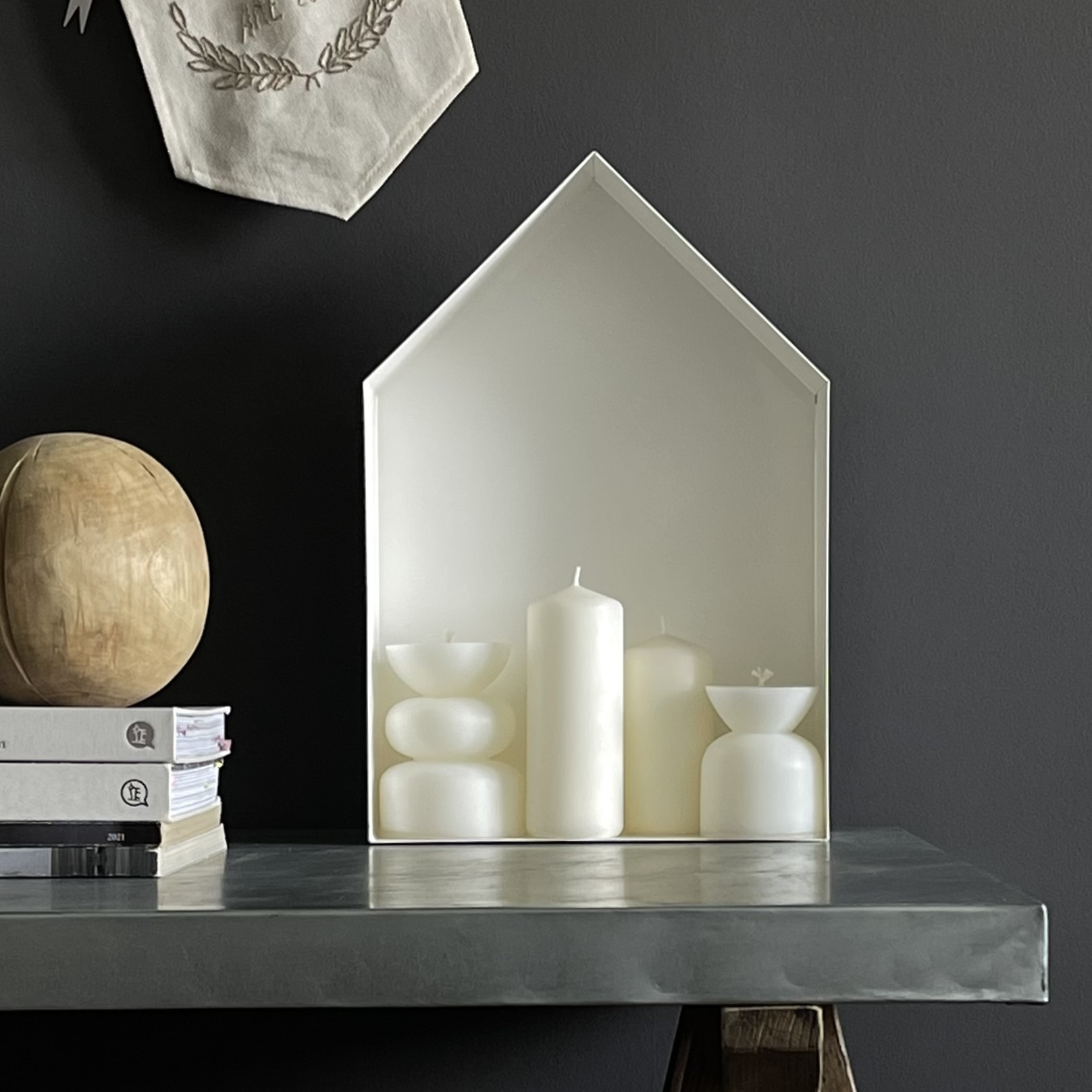 Полка в виде декоративного домика из стал стоит на столе на фоне графитовой стены.