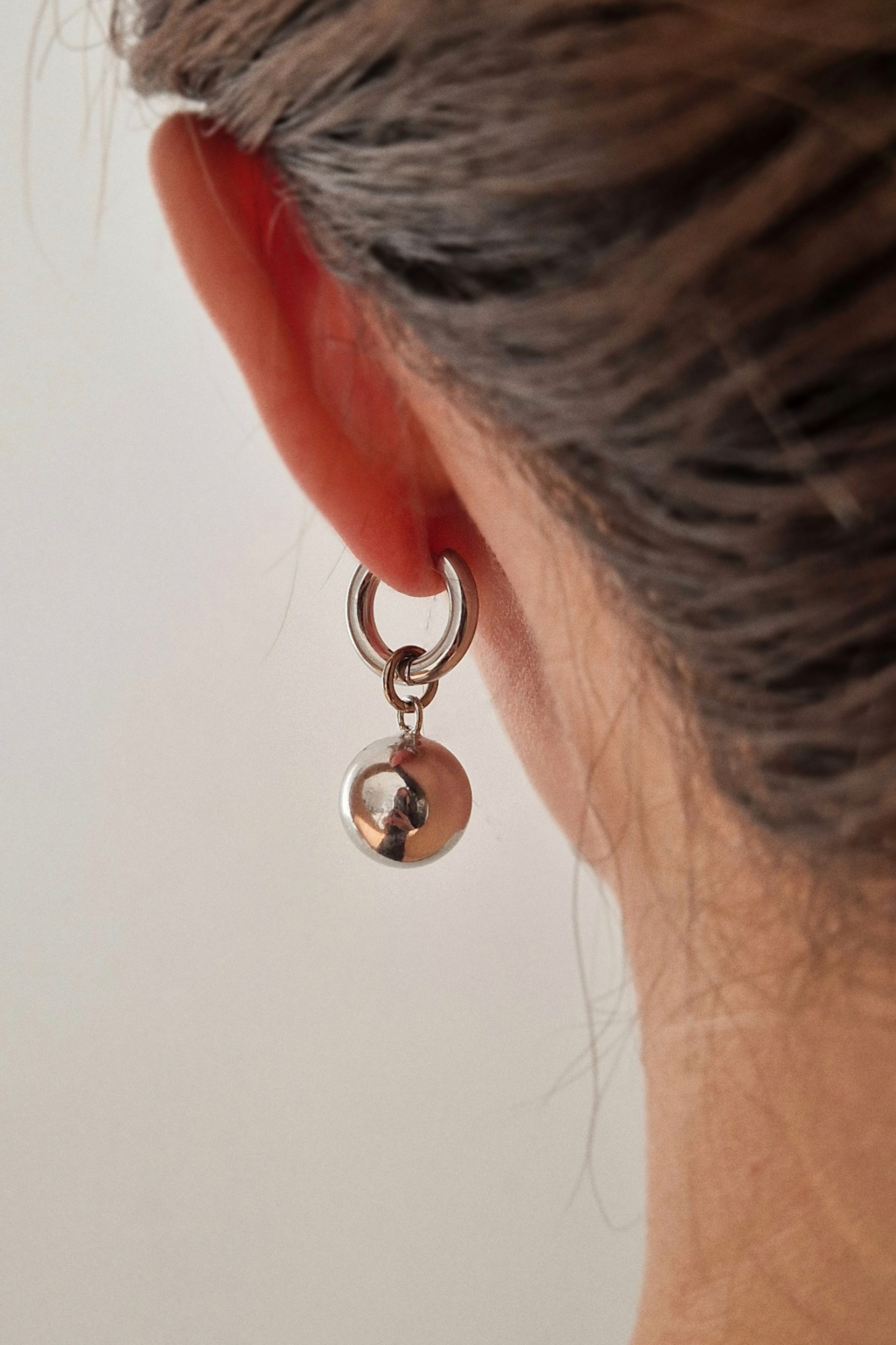 серебристые серьги с подвеской шариком на женском ухе