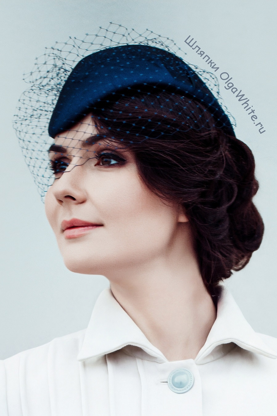 Синяя шляпка с вуалью и прической на девушке в светлом пальто с синей сумкой