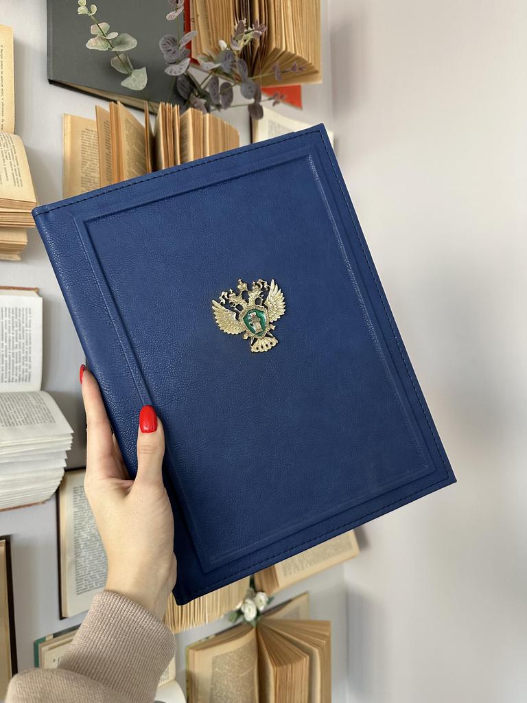 Папка на подпись в синей эко-коже с металлическим гербом Прокуратуры и фактурным бортиком по периметру. Строгий, официальный дизайн, символизирующий закон и справедливость.