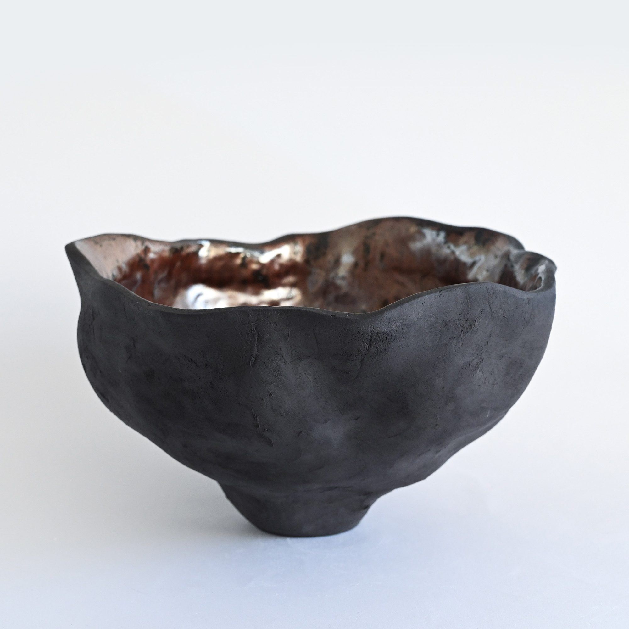 A black handmade textured vase with a metallic glaze and a wavy form