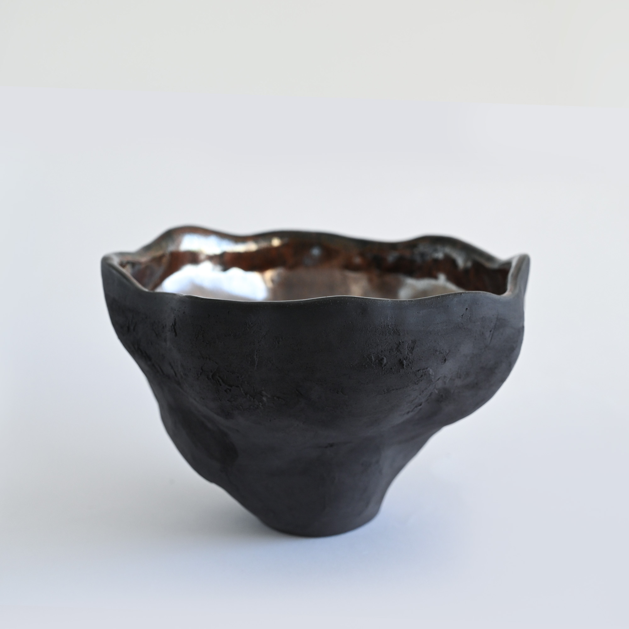 A black handmade textured vase with a metallic glaze and a wavy form